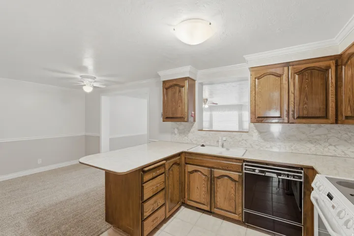 Kitchen featuring wood cabinetry, white countertops with integrated sink, and a black built-in dishwasher