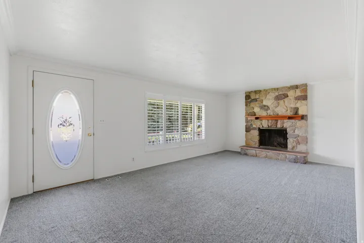 Living area featuring a stone-clad fireplace with a wood mantel, light gray carpet flooring, and white walls