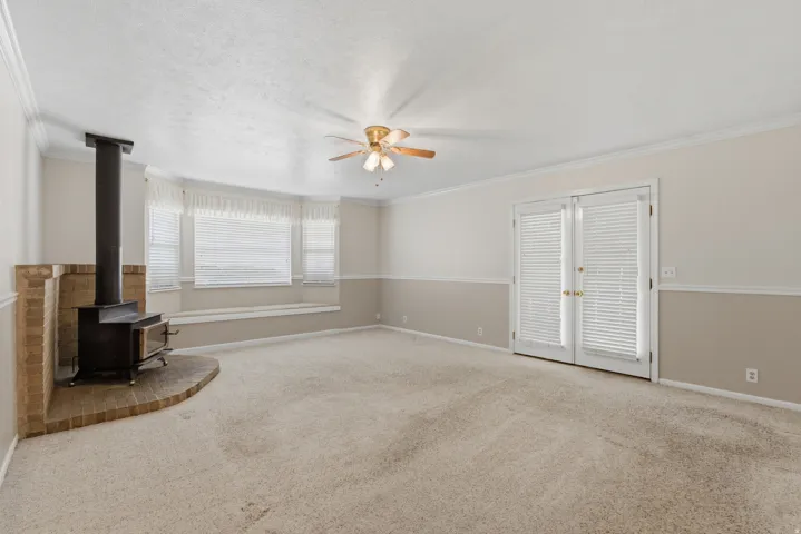 Expansive room featuring a brick-surround wood-burning stove, bay windows with integrated bench seating, neutral carpeting, a ceiling fan, and French doors