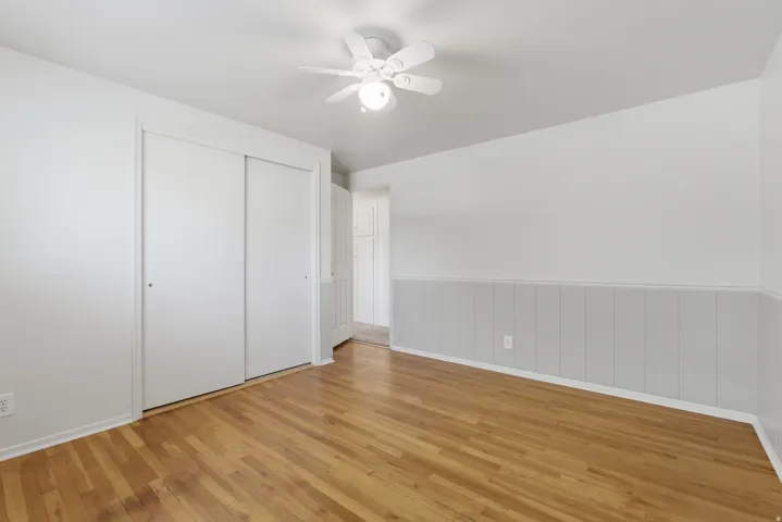 Room featuring wood-finish flooring, a ceiling fan with integrated lighting, and a partial panel wall treatment