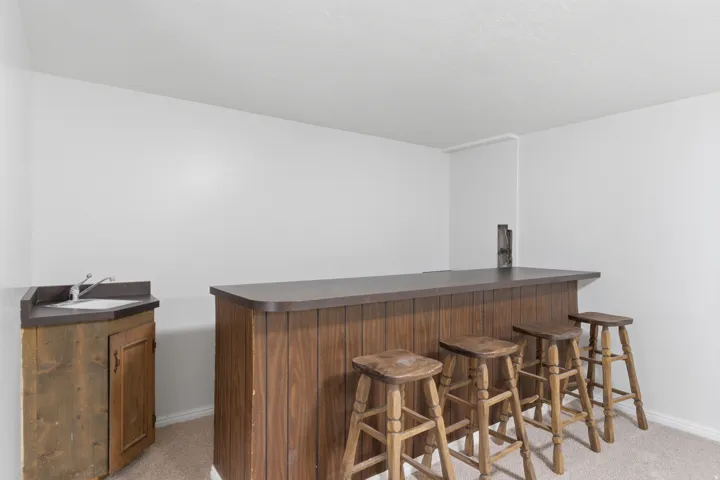 Built-in bar with wood-finish paneling, dark countertop, and integrated corner wet bar featuring a sink