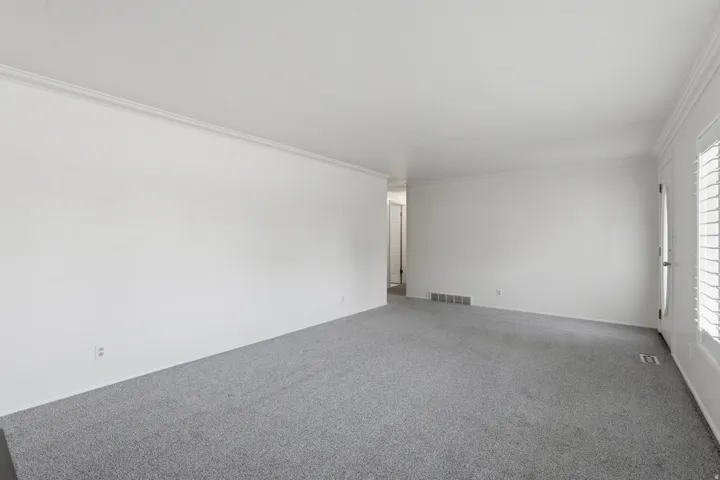 Spacious room featuring light gray carpeting, white walls, and crown molding