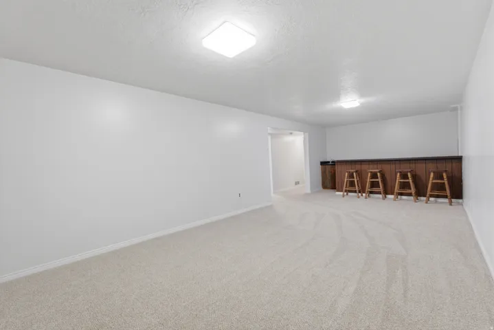 Spacious room featuring light-colored carpeting, white painted walls, and square ceiling light fixtures