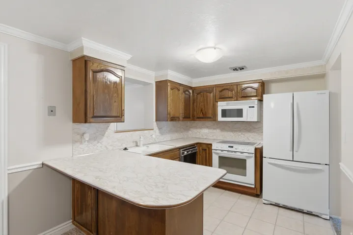 Kitchen featuring wood cabinetry, light-toned countertops, tile flooring, and white appliances including a refrigerator, range, and microwave