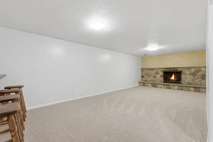 Spacious room featuring a stone-faced fireplace with a raised hearth, light-toned carpeting, and recessed ceiling lighting