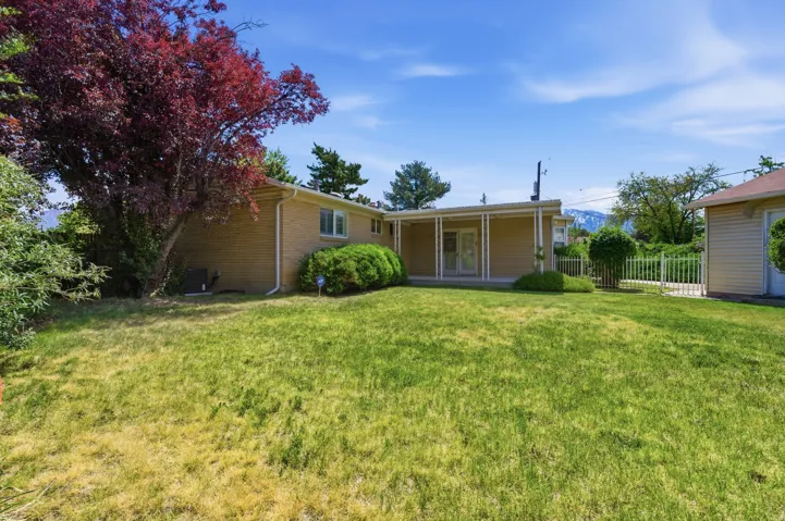 Expansive backyard featuring a covered patio, mature landscaping, brick exterior, white framed windows, and a detached structure