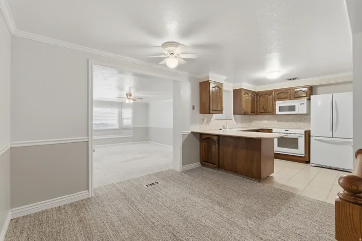 Kitchen featuring wood cabinetry and white appliances, with light-toned tile flooring