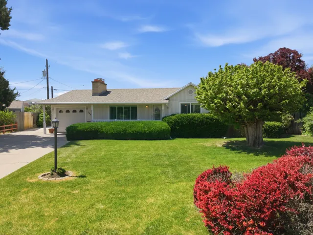 Single-story residence featuring a front lawn with mature trees and established landscaping