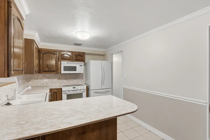 Spacious kitchen featuring a white countertop with a built-in sink, wood-finish cabinetry, and white appliances including a refrigerator, range, and microwave