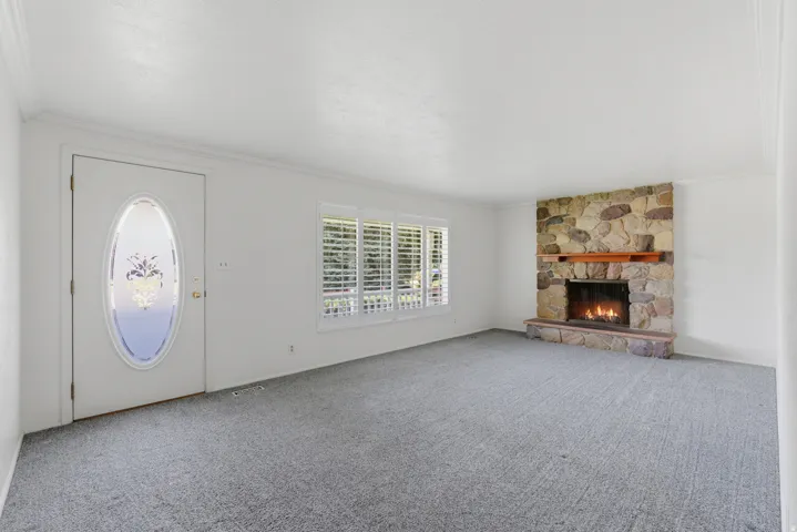 Living area featuring a stone-faced fireplace with a wood mantel, light gray carpeting, and white window shutters
