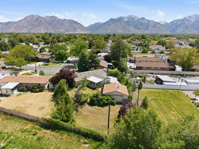 Expansive property with a large undeveloped lot, established trees and shrubs, and a distinct brown-roofed outbuilding