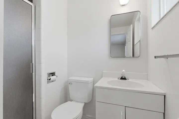 Compact bathroom featuring a shower with a frosted glass door, a toilet, a vanity with an integrated sink, a wall-mounted mirror, and a chrome towel bar