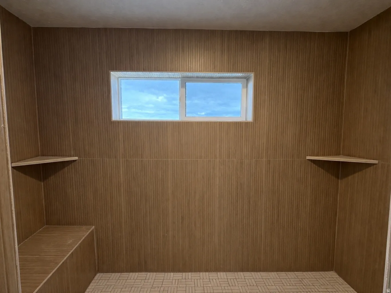 Primary ensuite walk-in shower featuring patterned tile flooring, wood-look wall tile, dual shower heads, a built-in shower bench, a corner shelf, and a frosted transom window