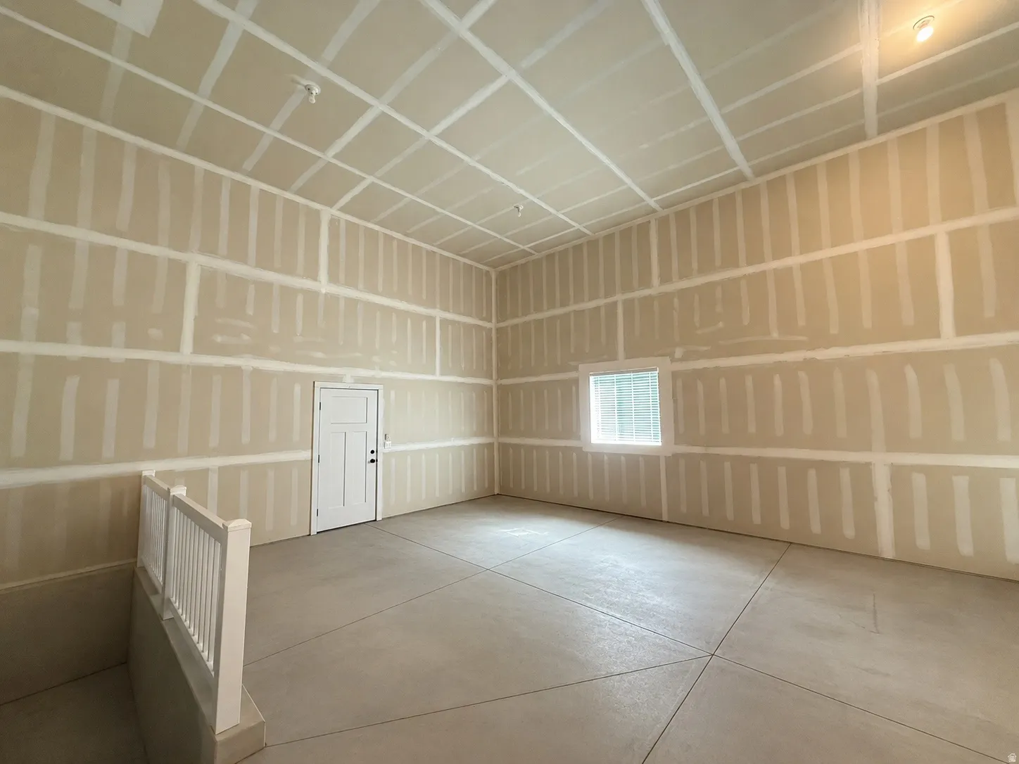 Unfinished interior space featuring high ceilings, exposed drywall, and concrete flooring