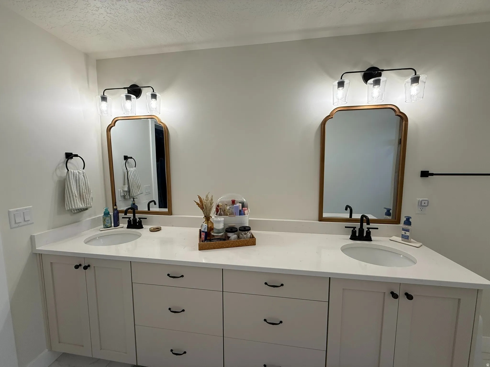 Primary ensuite dual vanity featuring white shaker-style cabinetry, white countertops, and black hardware