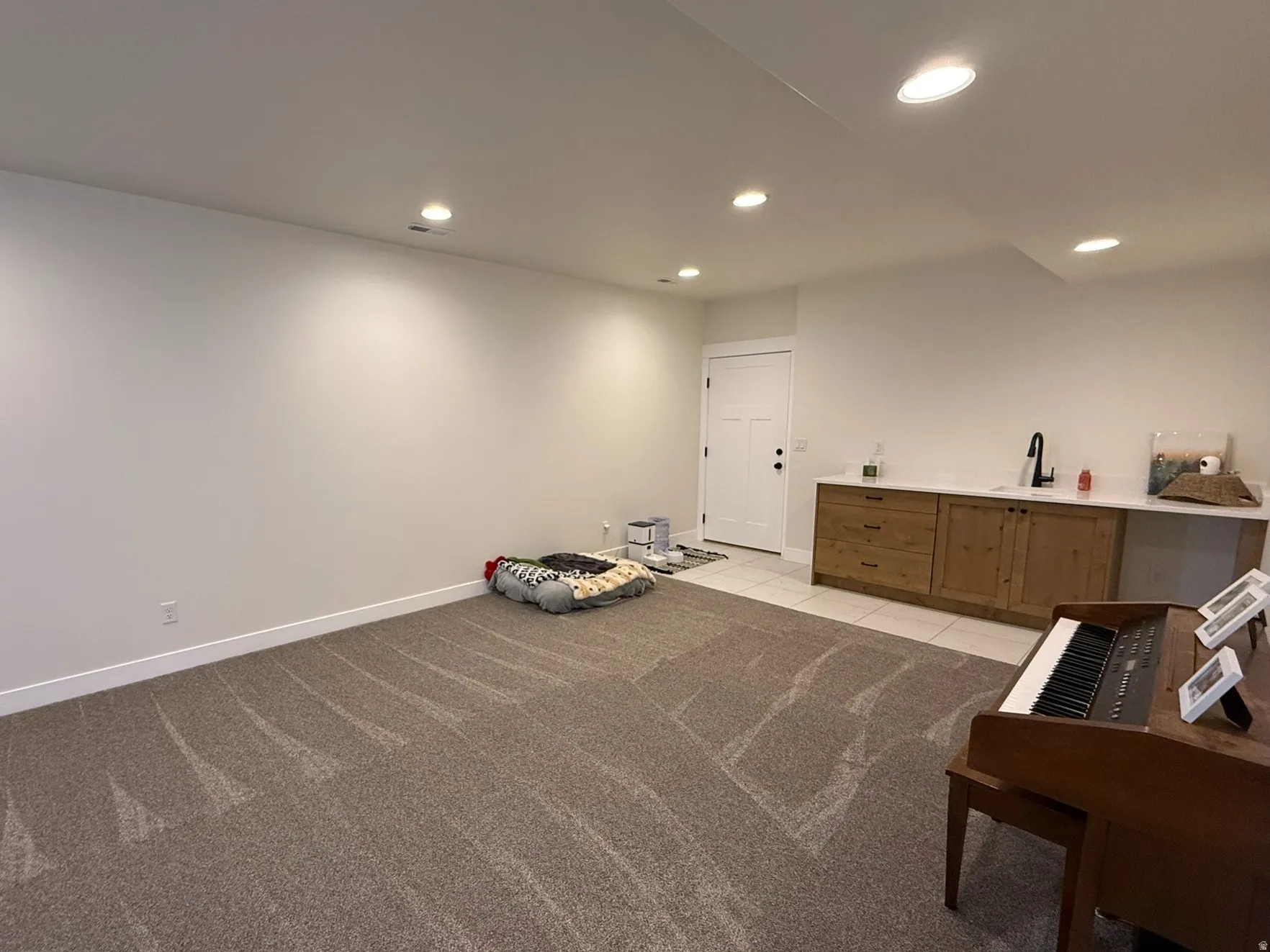 Family room featuring neutral carpeting, recessed lighting, and a built-in kitchenette with sink and space for mini-fridge with wood cabinetry and a light-toned countertop