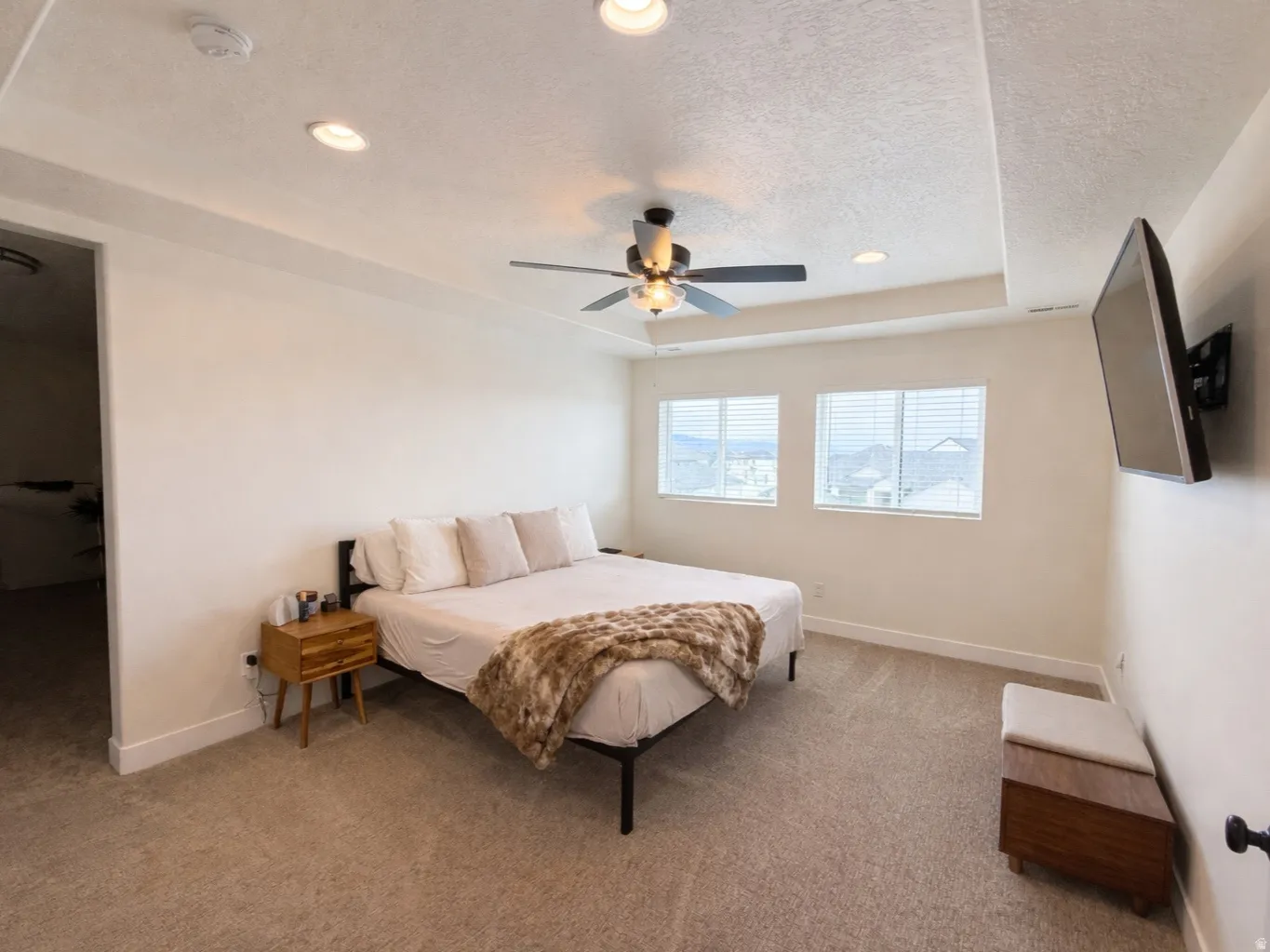 Primary bedroom featuring carpet, a tray ceiling with recessed lighting and a ceiling fan