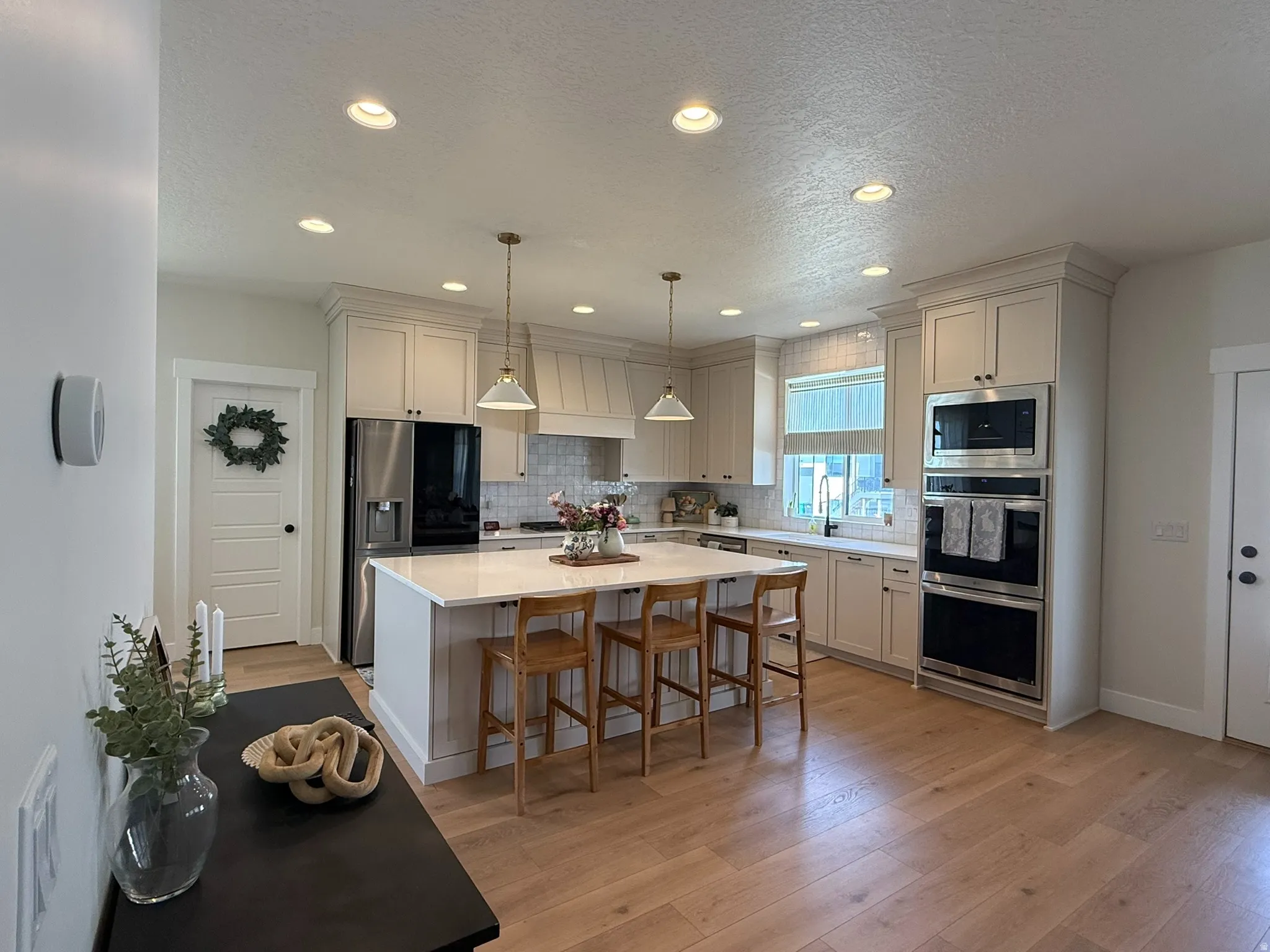 Open-concept kitchen featuring an oversized island with seating, pendant lighting, recessed ceiling lights, stainless steel appliances, and wood-finish flooring