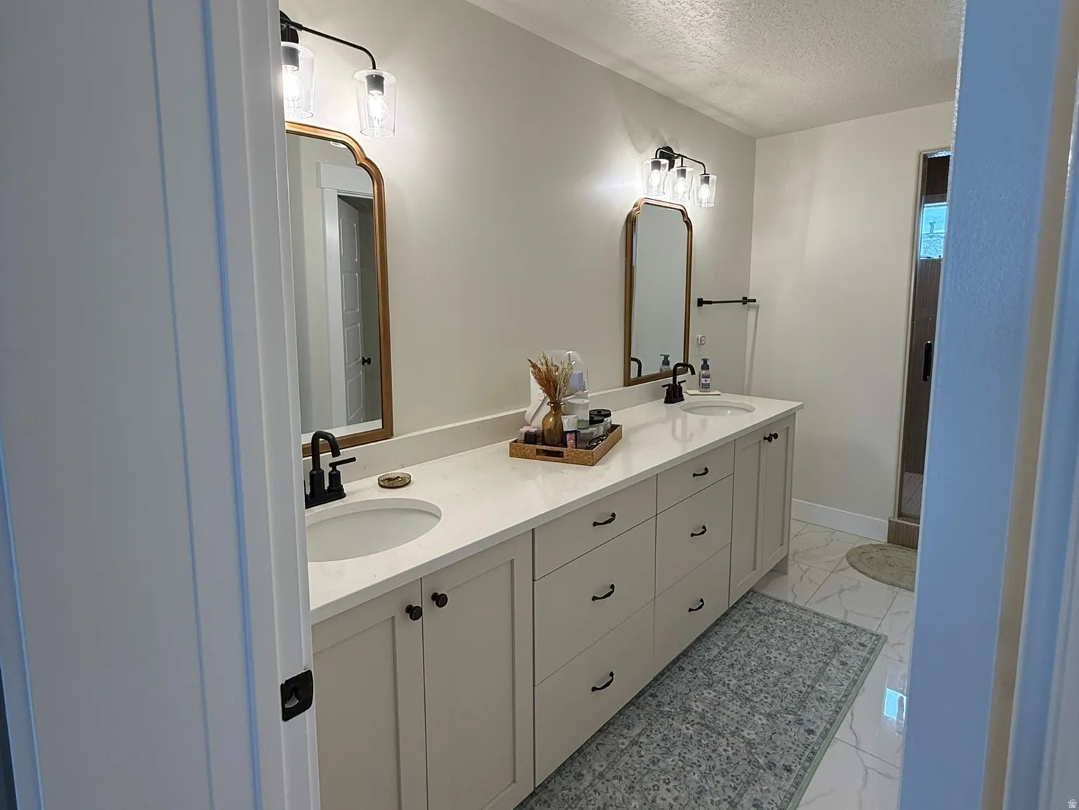 Primary ensuite dual vanity with light cabinetry and stone-finish countertops