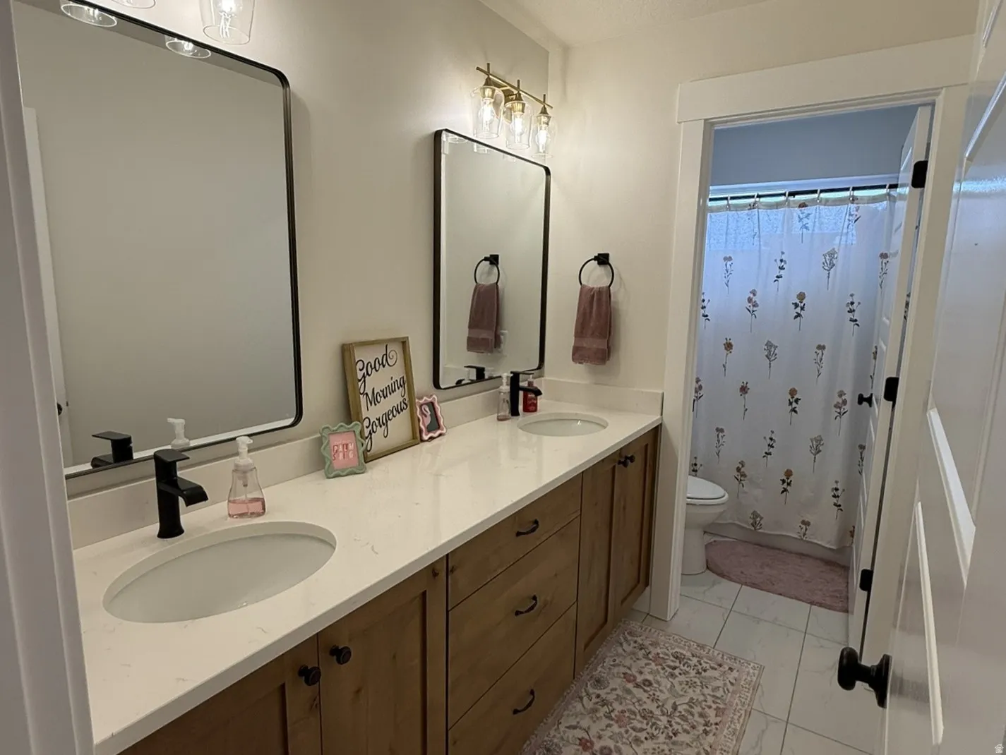 Guest bathroom with double vanity featuring wood-finish cabinetry, white countertops, and matte black fixtures