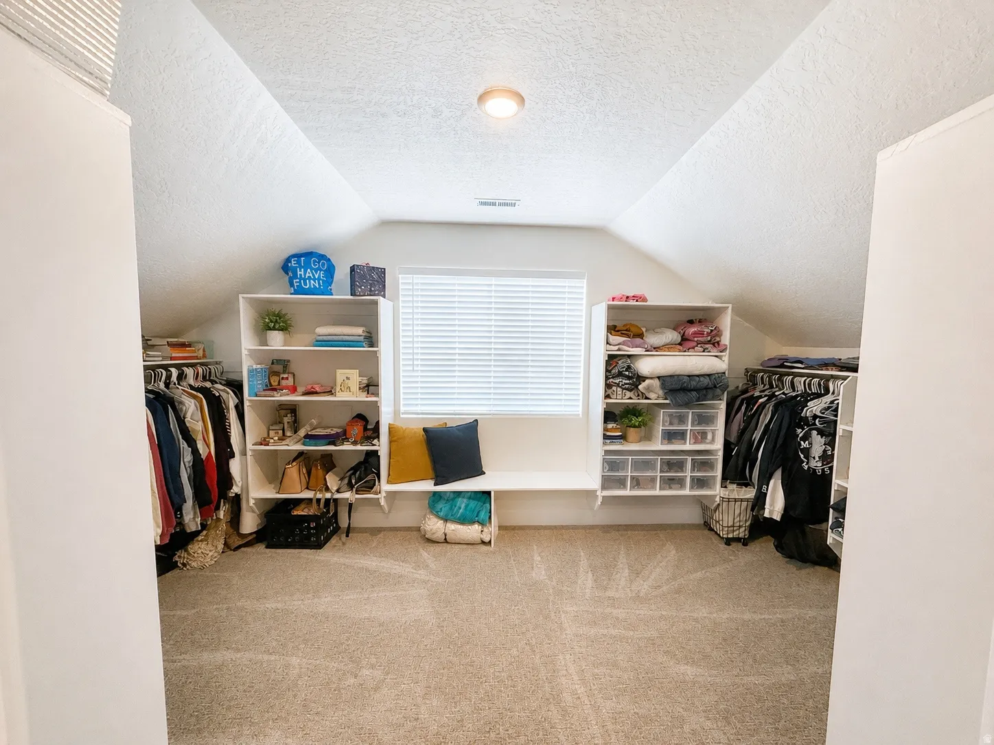 Primary bedroom walk-in closet featuring sloped ceilings, plush carpet flooring, a built-in window bench, and integrated shelving units