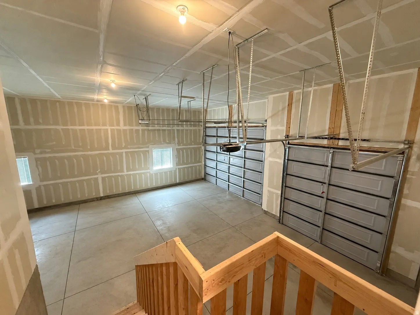 Spacious garage with exposed drywall, concrete flooring, two overhead garage doors, light fixtures, and windows providing natural light