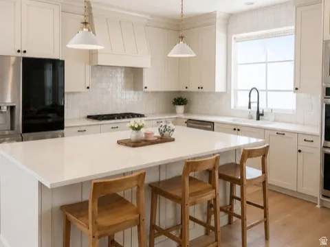 Kitchen featuring a large central island with seating, integrated sink, stainless steel appliances, white cabinetry with black hardware, and wood-finish flooring