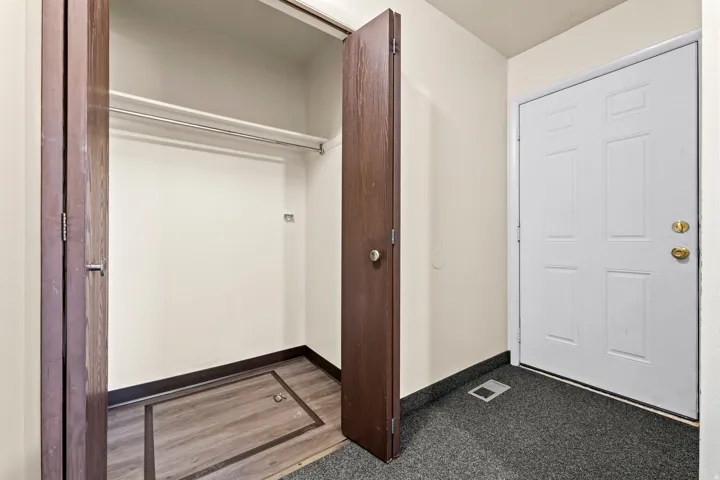 Entryway featuring a white paneled door with brass hardware, dark gray carpet flooring, and a built-in closet with wood-finish bi-fold doors, hanging rod, and wood-finish flooring