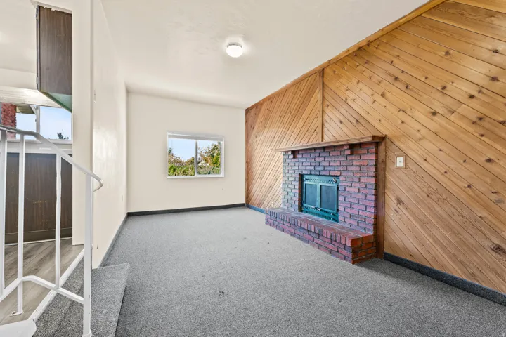 Living area with a prominent brick fireplace, wood paneling, and a single window