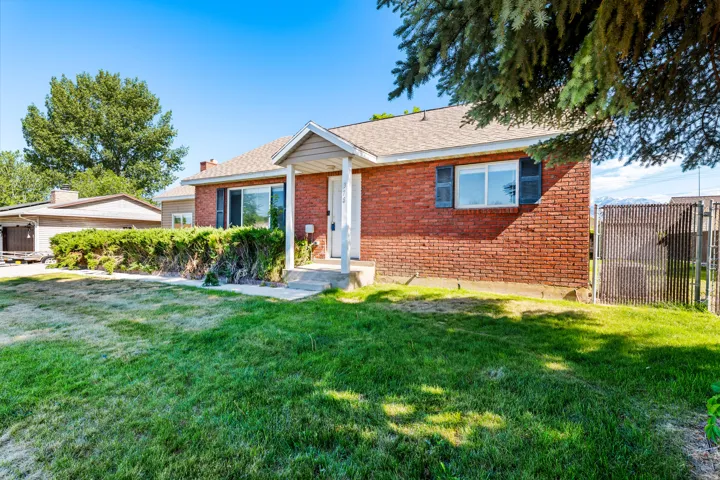 Brick exterior featuring a covered porch entry, multiple windows with shutters, and a fenced side yard