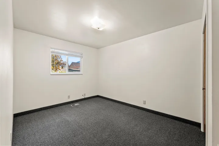 Room featuring light-toned walls, dark gray carpeting, and a white-framed window