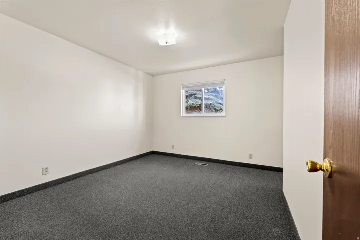 Room featuring a neutral wall color, dark gray carpet, white trim, and a window with exterior visibility