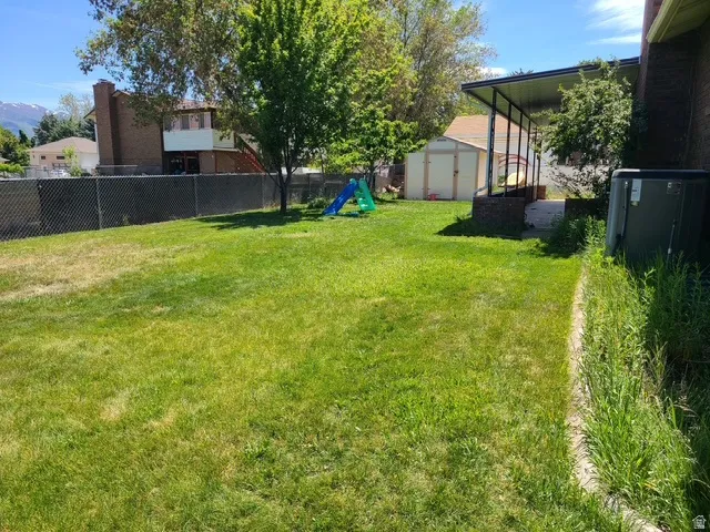 Expansive grassy lawn with a chain-link fence, mature trees, and a detached storage shed