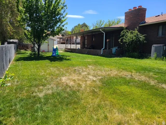 Expansive rear yard featuring mature trees, a chain-link fence, and a brick exterior with a covered patio