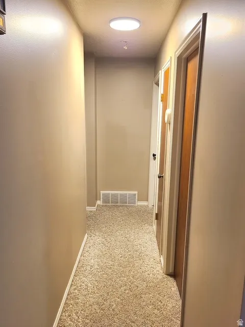 Hallway featuring neutral carpet flooring, light beige wall paint, white baseboards, and a circular flush-mount ceiling light
