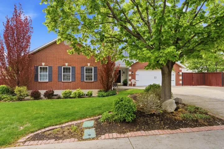 Brick facade residence featuring a two-car garage, mature landscaping, and a paved driveway