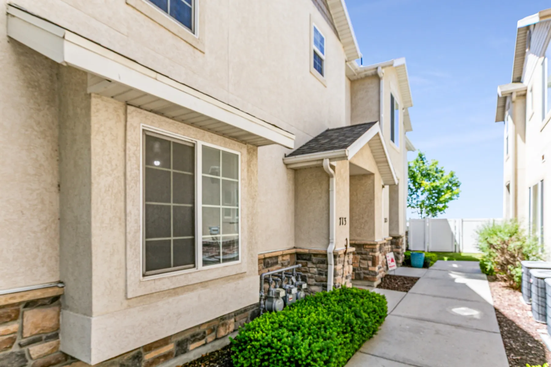 Stucco exterior featuring stone veneer accents, a covered entry, and a pitched roofline