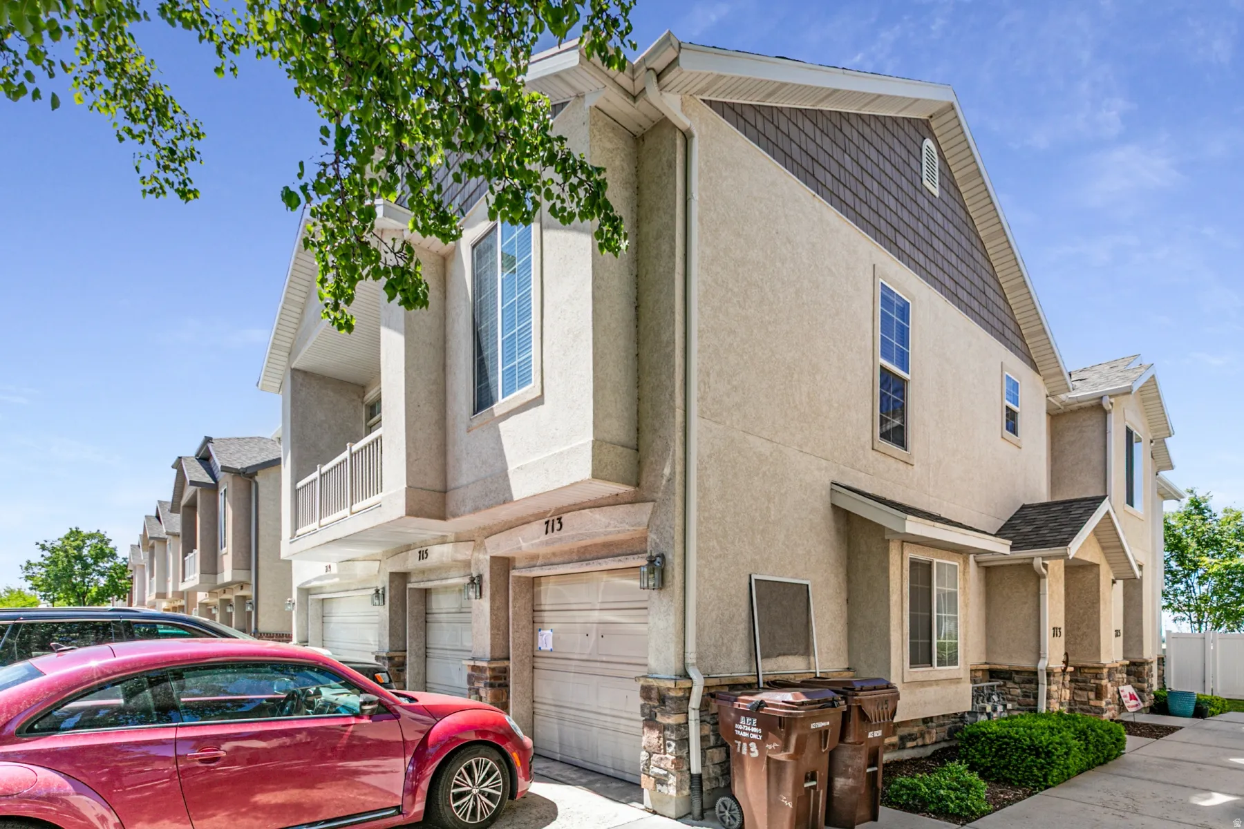 Contemporary townhome exterior featuring light-colored stucco siding, dark shake shingles on the gables, and stone veneer accents
