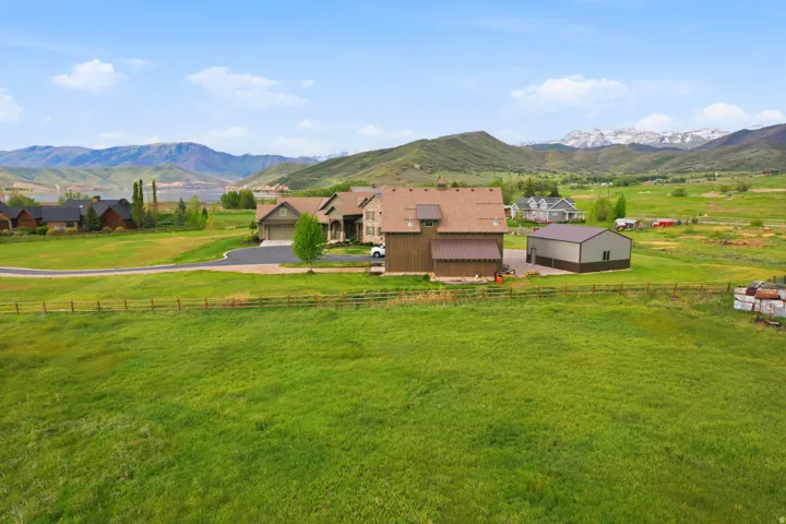 Expansive green landscape featuring a multi-level home with an attached garage, a separate barn-style structure, and an additional metal-sided outbuilding
