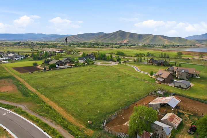 Expansive property featuring a large green field, surrounding residential structures, a visible body of water, and distant mountains