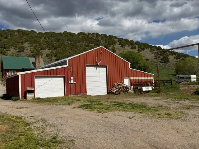Red metal barn featuring two white garage doors, a pedestrian entry door, and a white trim accent