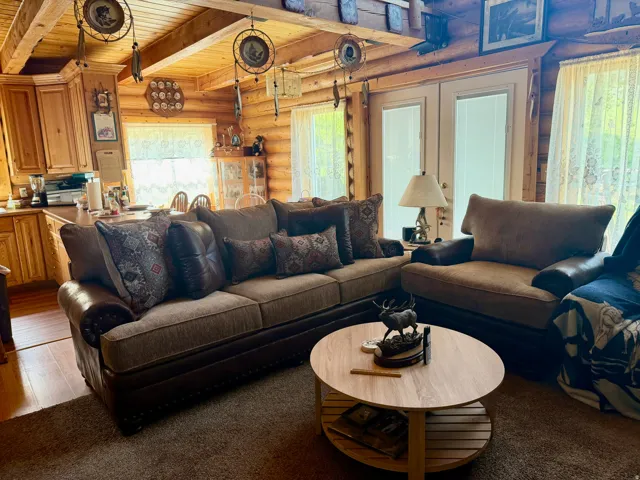 Open-concept living area featuring log walls, exposed wood beam ceilings, wood-finish flooring, and light oak cabinetry