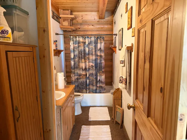 Bathroom featuring wood-finish paneling, a full bathtub with shower, a single vanity with an integrated sink, and an exposed wood beam ceiling