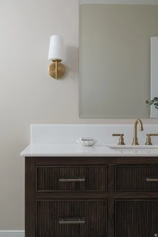Bathroom vanity featuring a dark wood finish with reeded detailing, white countertop, and gold-toned faucet