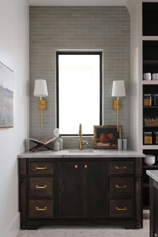 Dark wood vanity featuring brass hardware, a white countertop, and an undermount sink with a brass faucet