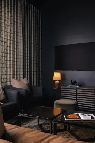 Dark-toned room featuring a large mounted display, full-height drapery, and dark walls