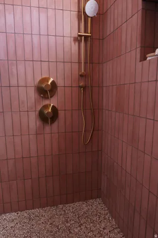 Shower with vertical subway tile in a terracotta hue, featuring brass fixtures including a rain shower head and handheld sprayer