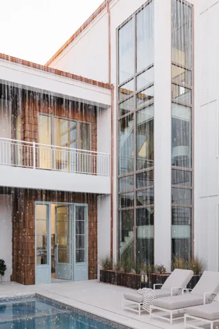 Contemporary exterior featuring a multi-story glass facade, a private balcony with white railing, wood shingle accents, and a swimming pool with surrounding patio