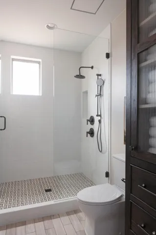 Frameless glass shower enclosure featuring white subway tile walls and a basketweave tile floor