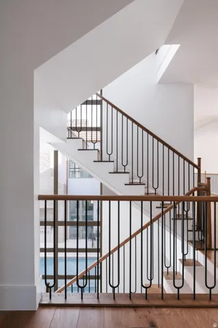 Multilevel staircase featuring black metal balusters with unique u-shaped elements and light wood handrails